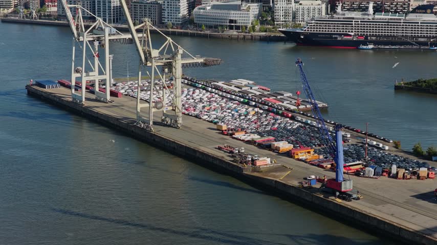 Aerial view tilting up from harbor cranes on a car terminal to reveal the HafenCity waterfront and city skyline of Hamburg, Germany, with TV tower and church spires
