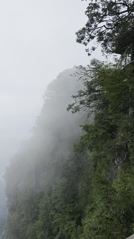 Mist and low clouds drifting across the steep forested cliffs of Tianmen Mountain in Zhangjiajie, Hunan, China.