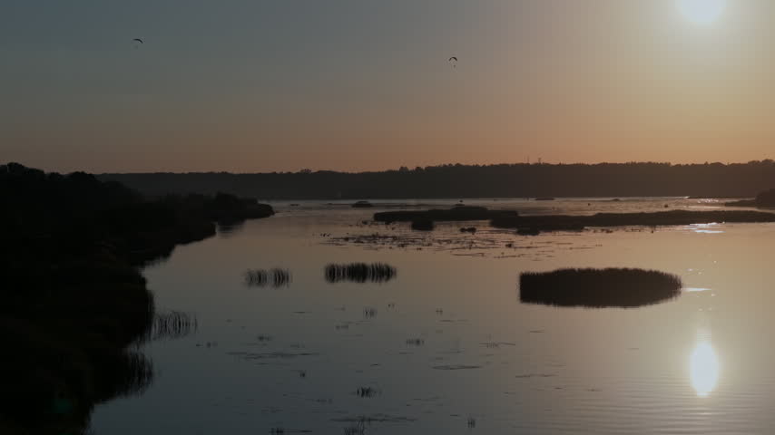 Wild river at sunset in early autumn with paragliders flying above and golden reflections.