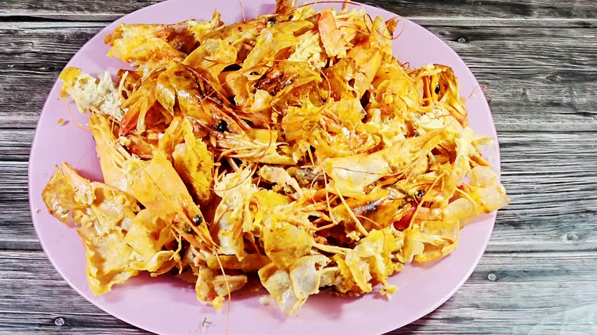 a pile of discarded shrimp or prawn shells, heads, and tails on a light purple plate, representing seafood waste from a meal or food preparation