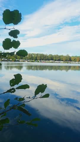 Scenic blue sky and clouds reflecting on calm lake water with tree branch framing