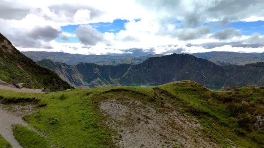 Aerial view of the turquoise Quilotoa Lake crater surrounded by steep volcanic walls and lush green slopes under a cloudy sky in Cotopaxi, Ecuador.
