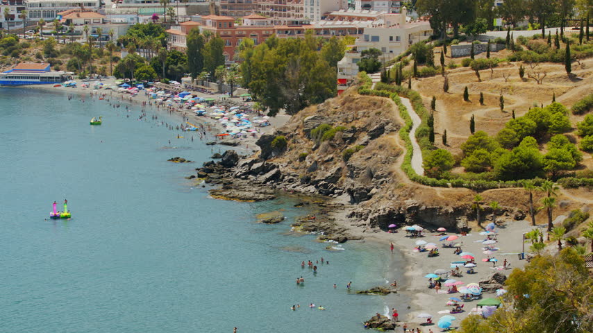 Scenic panoramic view of Costa Tropical coast in Almunecar, Spain. Beautiful Mediterranean sea bay crowded with tourists and vacationers relaxing on a sandy beach during summer holidays. Sunny daytime landscape 