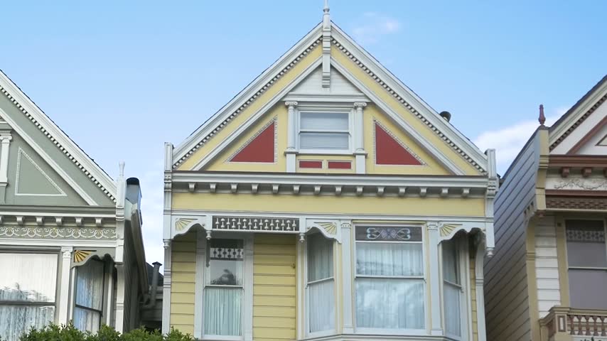 Aerial view of a yellow Victorian house with ornate woodwork and red accents in San Francisco, California, United States.