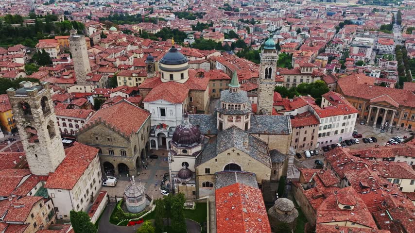 Aerial drone view of Basilica di Santa Maria Maggiore and Bergamo Cathedral in Bergamo, Italy, showcasing historic churches, domes, bell towers, ornate architecture, and the medieval Città Alta.