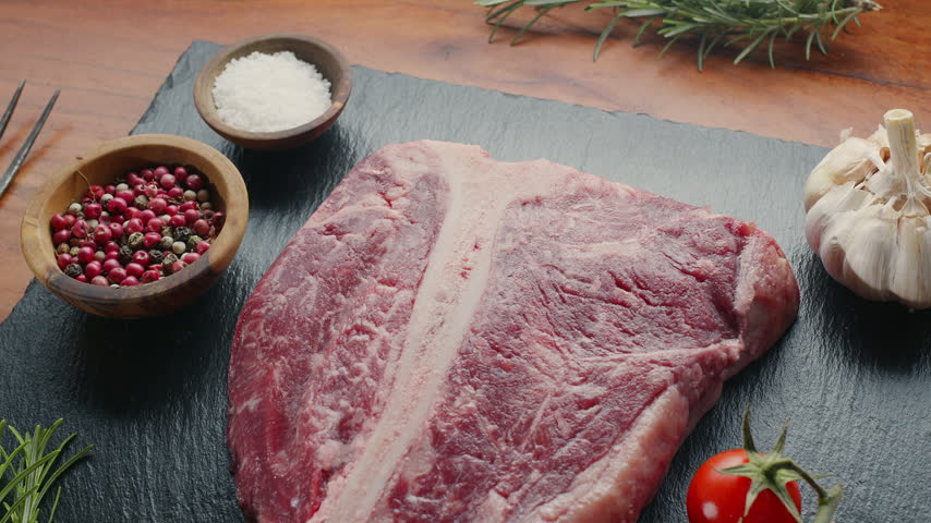 Raw T-bone steak with herbs and garlic and tomatoes on the serving slate board close-up. Top view.