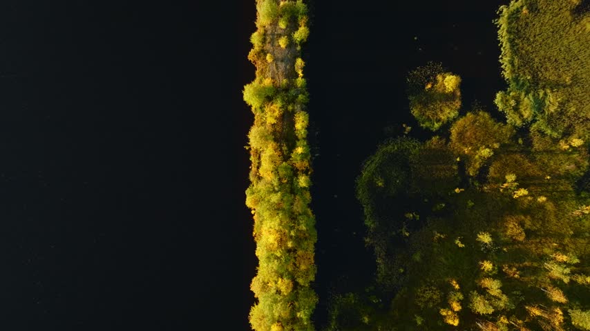 Aerial view of a narrow, tree-lined strip of land surrounded by dark water in the wilderness of Peurasuvanto, Lappi, Finland.