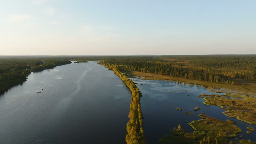 Aerial view of the Peurasuvanto river winding through the vast coniferous forests and wetlands of Finnish Lapland under a clear sky in Peurasuvanto, Lappi, Finland.