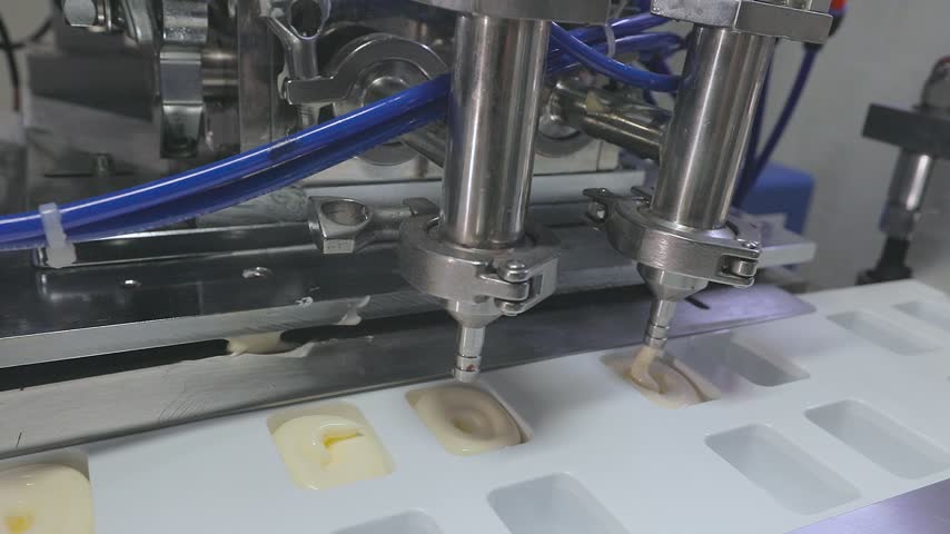 Close-up of an automated industrial liquid and sauce filling machine dosing mayonnaise into plastic portion cups dip pot on a conveyor belt. Plant for production of mayonnaise and sauce. 