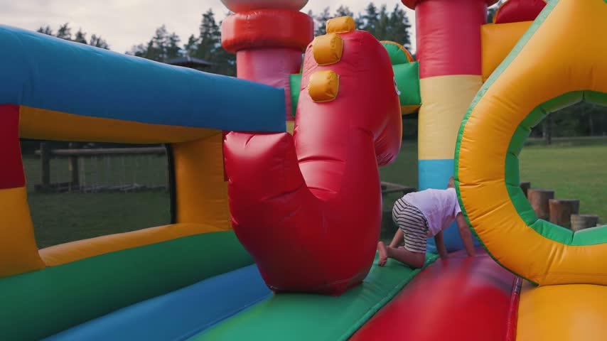 Two boys engage in playful activities on a bright inflatable bounce house, sliding down and exploring colorful tunnels in a lively outdoor environment
