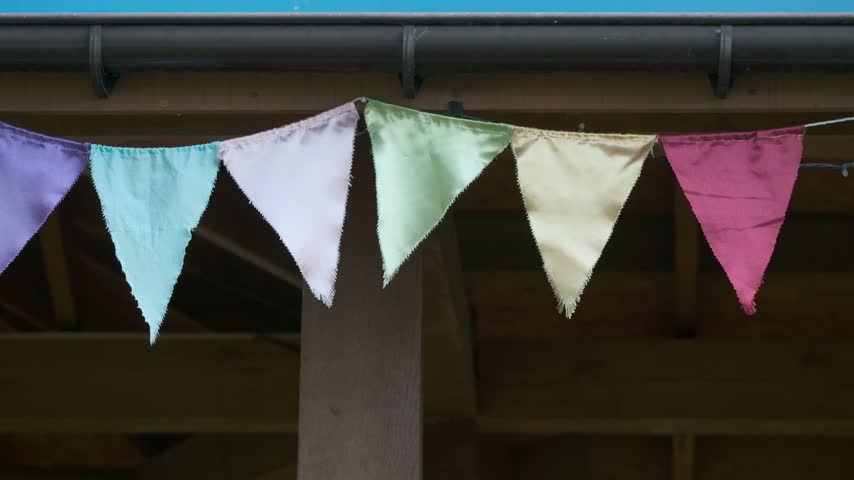 Colorful triangular bunting flutters gently beneath a wooden garden shelter.