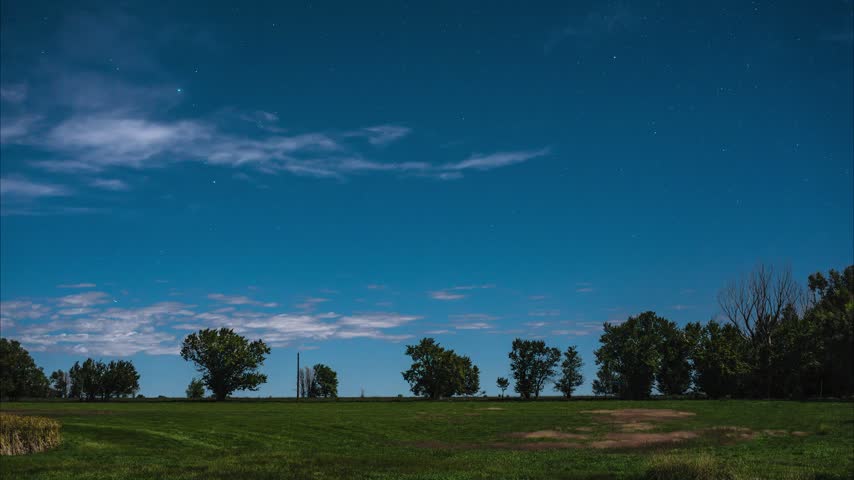Full moon turns night into day on this late night timelapse over a rural farm and ranch.  Stars rise over the tree lined horizon as clouds move, appear, and fade with the occasional jet plane passing by.