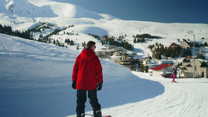 A person in a red jacket snowboards down a snowy mountain slope. Enjoying winter sports and recreation at a beautiful ski resort.