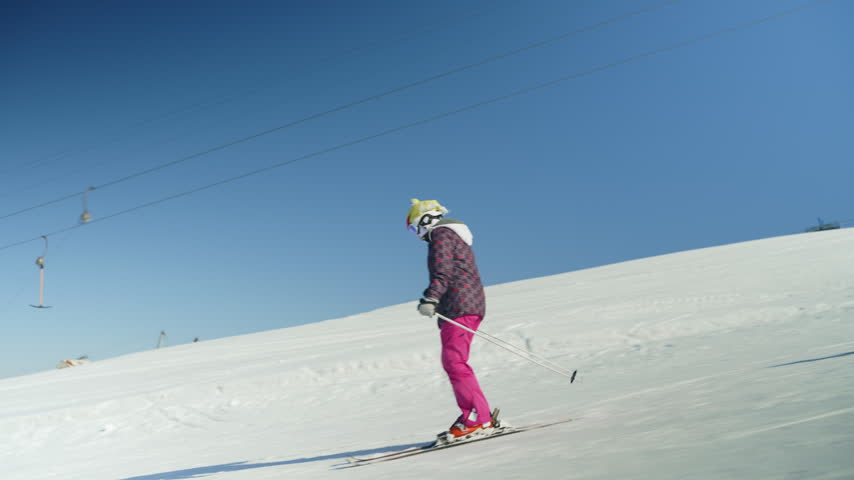 A young girl skis down a sunny, snowy mountain slope while a man snowboards nearby. Enjoying winter sports, they descend the piste together at a vibrant ski resort.