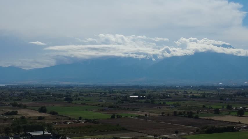 Aerial view of the majestic Mount Olympus partially covered by clouds above the agricultural plains of Paralia Katerinis, Pieria, Greece.