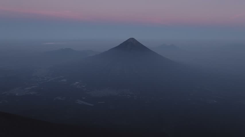 Aerial view of Volcan de Fuego rising above the landscape at dusk with soft purple light over the horizon in Yepocapa, Chimaltenango Department, Guatemala.