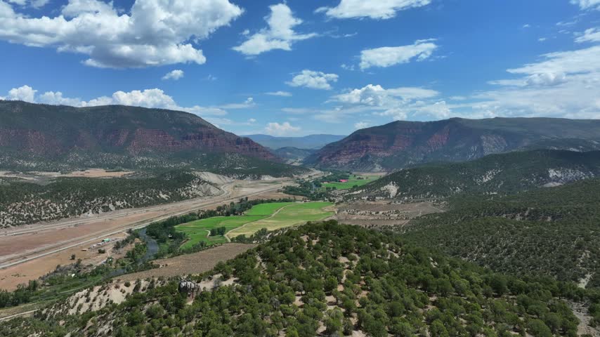 Aerial view of the lower valley in Eagle, Colorado, United States, featuring the Eagle River, Interstate 70, lush green fields, and rugged mountains in the distance.
