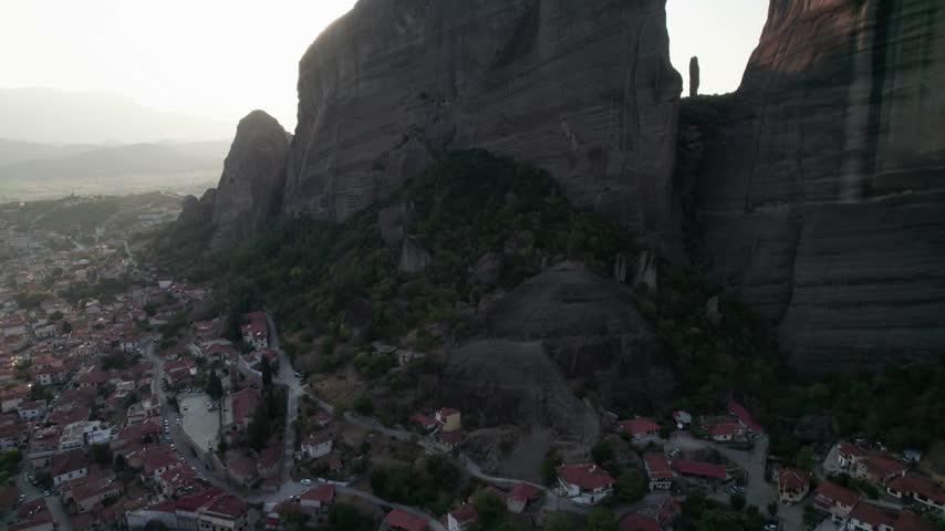 Aerial view of the dramatic Meteora rock formations towering over the town of Trikala with red-roofed houses and winding roads in Trikala, Greece.