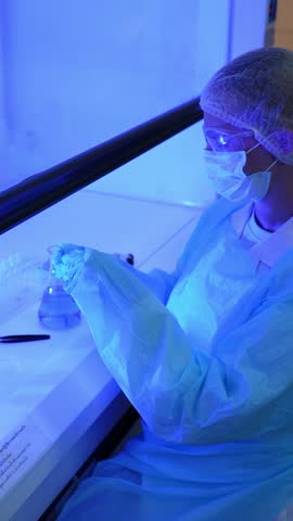 Vertical laboratory safety scene for social media: seated at a blue-lit biosafety cabinet, a researcher in full protective gear handles a glass slide, then pipettes a sample.