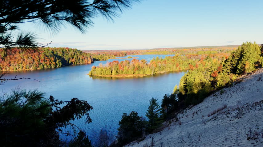 Scenic autumn view of a blue lake and forested island framed by pine branches from an elevated rocky overlook.