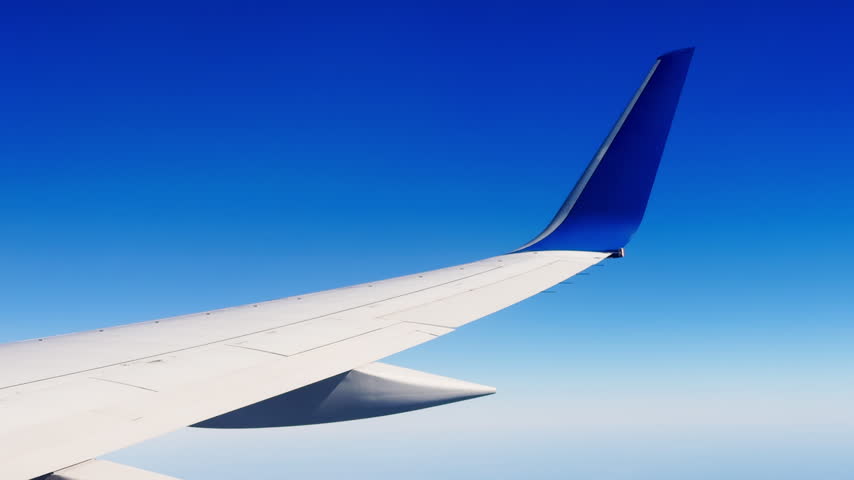 Minimal passenger airplane wing seen through a window against an expansive clear blue sky at cruising altitude.