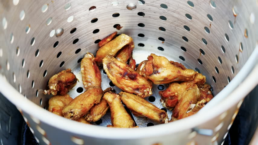 Close-up of golden fried chicken wings resting in a perforated metal basket after deep frying outdoors.