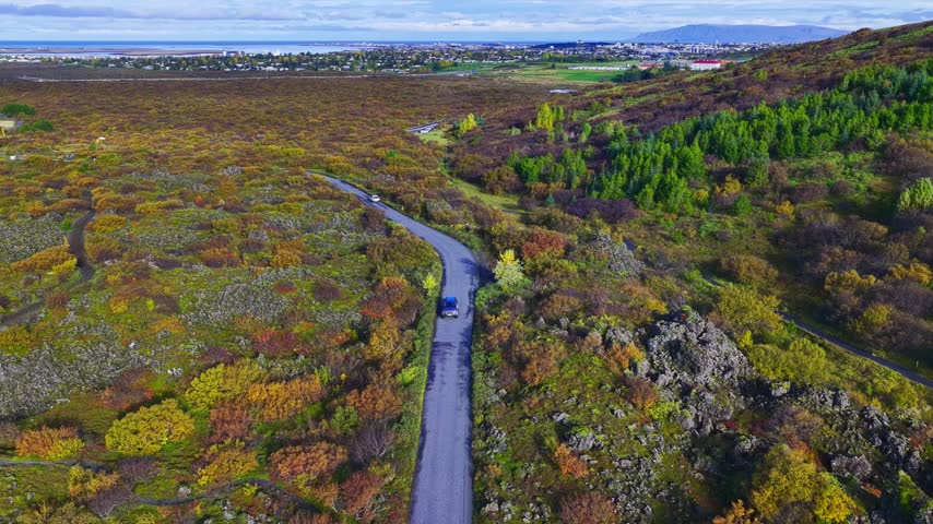 Aerial view of a road winding through a vibrant landscape with autumn colors and volcanic rock formations in Iceland.