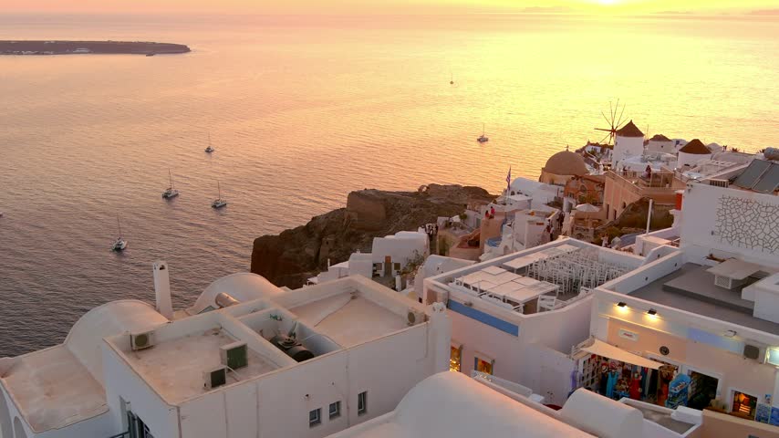 Aerial view of Oia with iconic white buildings and windmills overlooking the Aegean Sea at sunset in Oia, Cyclades, Greece.