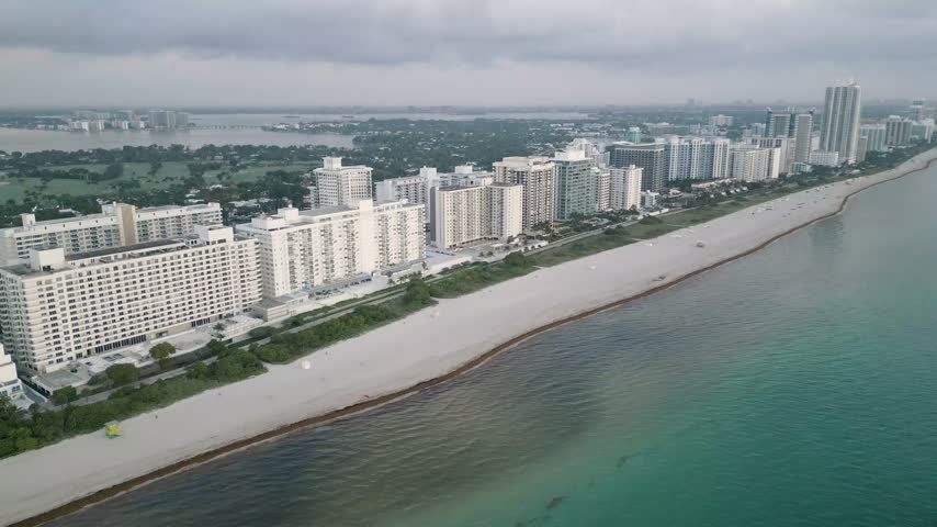 Aerial view of the Miami Beach coastline featuring high-rise residential buildings along the sandy shore and the turquoise Atlantic Ocean in Miami Beach, Florida, United States.