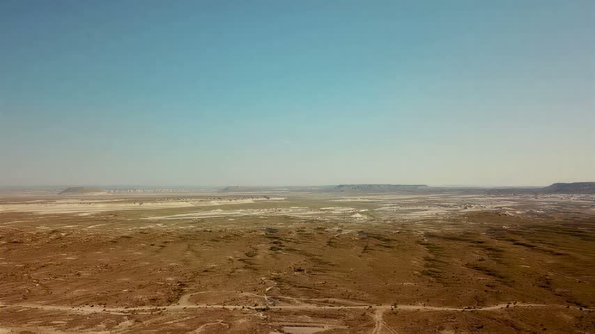 A wide panoramic perspective captures the expansive dry terrain and rugged geological formations stretching toward the distant hazy horizon line