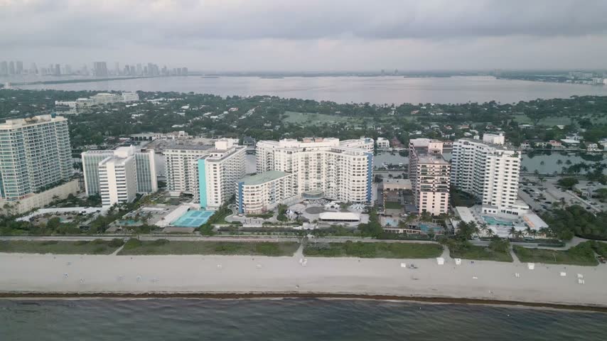 Aerial view of Miami Beach coastline featuring high-rise hotels and resorts along the sandy shore under a cloudy sky in Miami Beach, Florida, United States.