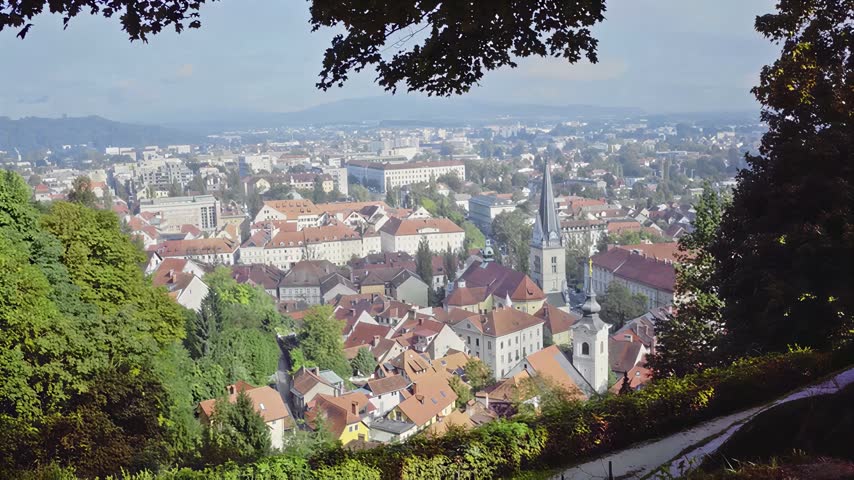 A high angle perspective overlooking the urban landscape of a European capital city featuring terracotta rooftops and a prominent church spire