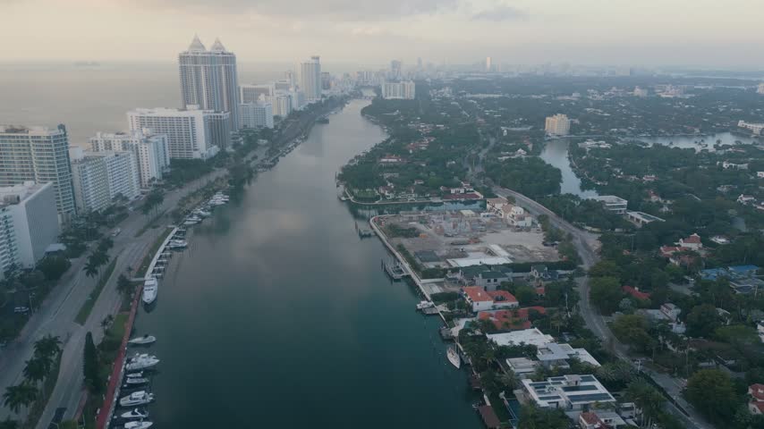 Aerial view of the Miami Beach waterway lined with high-rise buildings, residential homes, and docked boats under a hazy sky in Miami Beach, Florida, United States.