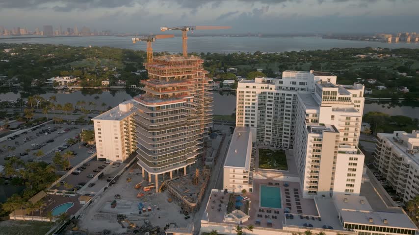 Aerial view of a high-rise building under construction with cranes and surrounding residential complexes in Miami Beach, Florida, United States.