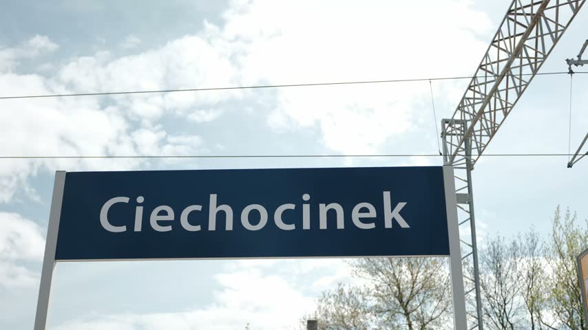 Blue train station sign with the name of the town Ciechocinek against a bright cloudy sky