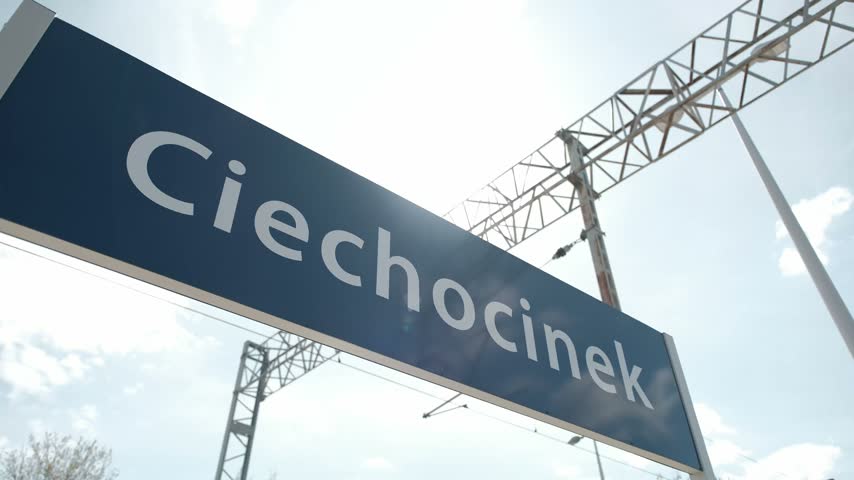 Blue train station sign with the town name Ciechocinek against a bright cloudy sky
