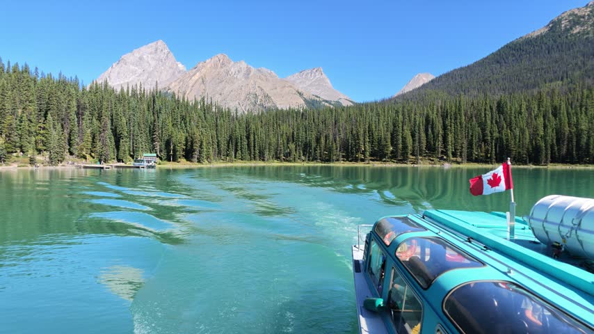 Tour boat cruising on Maligne Lake with Spirit Island, surrounded by dense evergreen forests and towering Rocky Mountains on a sunny summer day in Alberta, Canada in Jasper National Park