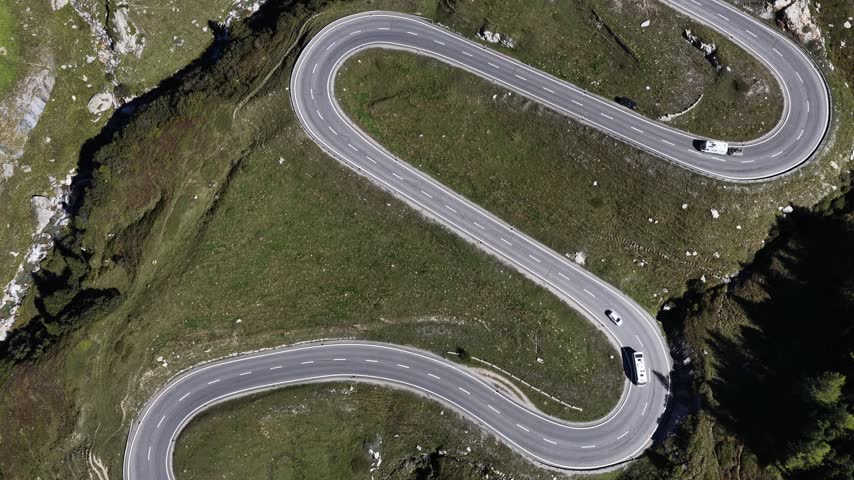 Aerial view of the winding Julier Pass road leading towards Silvaplana with cars driving through the alpine landscape in Surses, Grisons, Switzerland.