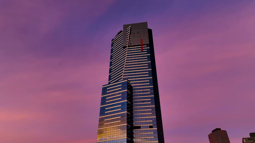 Aerial view of the modern Eureka Tower skyscraper with its glass facade reflecting the vibrant purple sunset sky in Melbourne, Victoria, Australia.
