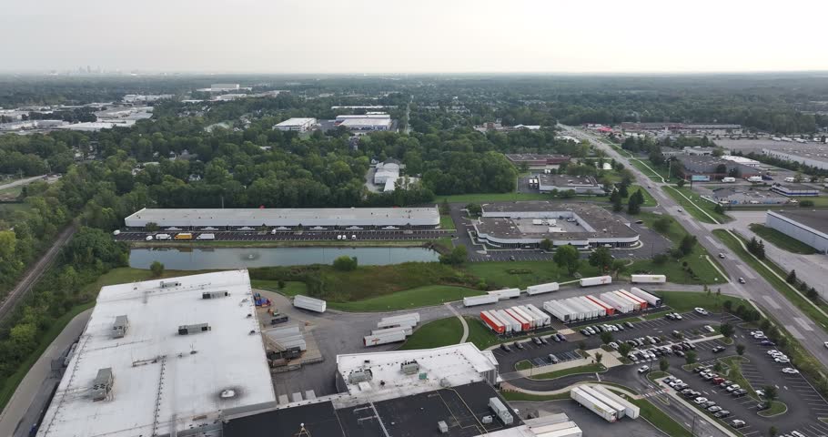 Aerial view of an industrial logistics park featuring large warehouses, loading docks with numerous semi-trucks, a small pond, and surrounding greenery in Indianapolis, Indiana, United States.