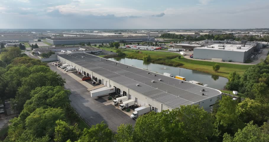 Aerial view of large industrial warehouse complex with loading docks and semi-trucks near a pond in Indianapolis, Indiana, United States.