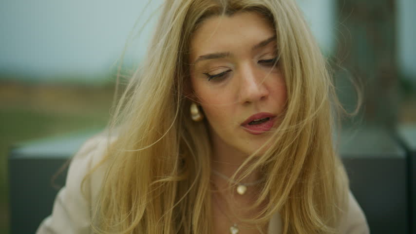 A happy blonde woman smiles outdoors with her hair blowing in the wind. Her joyful expression conveys a carefree and relaxed spirit.