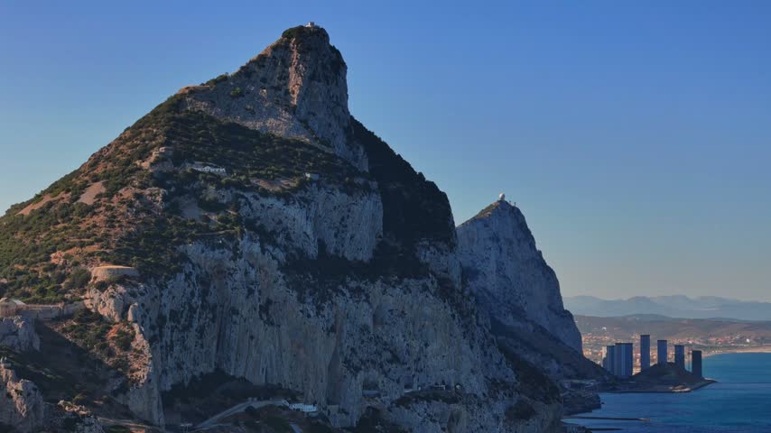 Aerial view of the Rock of Gibraltar with steep limestone cliffs, Mediterranean sea, and clear blue sky in Gibraltar, Gibraltar.