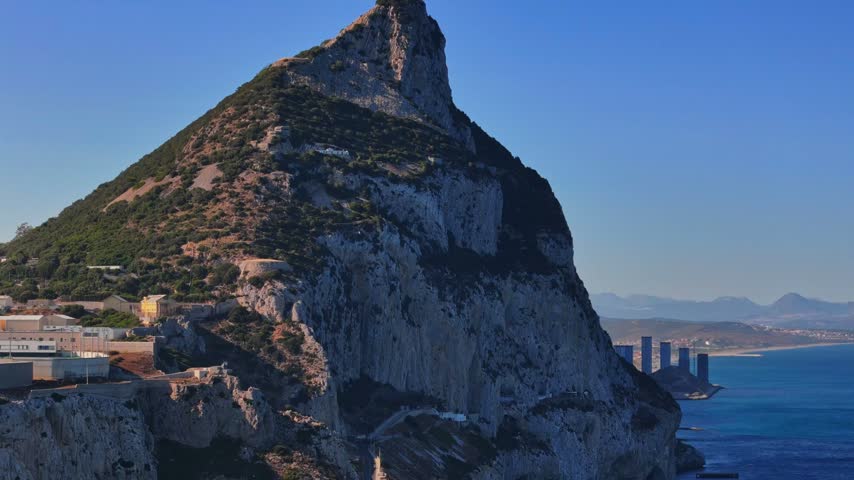 Aerial view of the iconic Rock of Gibraltar rising above the Mediterranean Sea with coastal urban developments and clear blue sky in Gibraltar, Gibraltar.