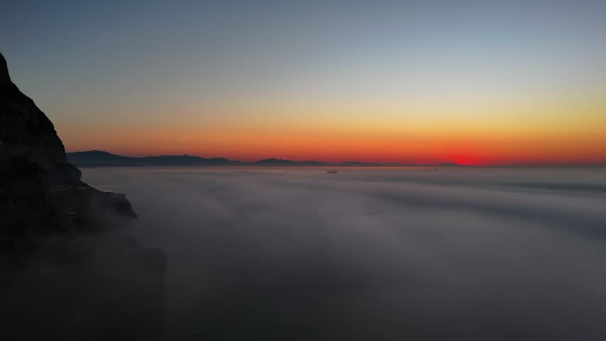Aerial view of Europa Point at sunset with thick fog rolling over the sea and dramatic orange sky in Gibraltar, Gibraltar.