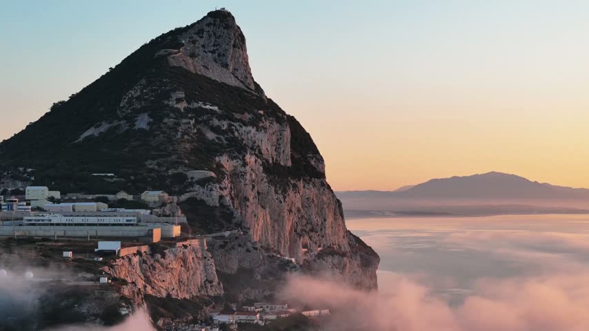 Aerial view of the iconic Rock of Gibraltar rising above the clouds during a golden sunset, Gibraltar, Gibraltar.