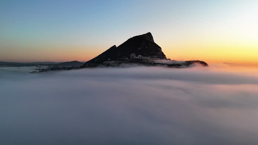 Aerial view of the Rock of Gibraltar rising above a thick layer of sea fog during a vibrant sunset in Gibraltar, Gibraltar.