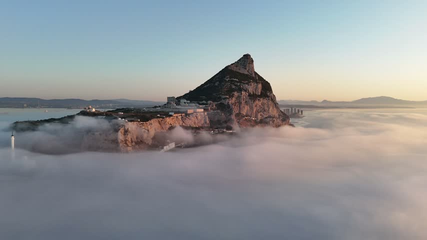 Aerial view of the Rock of Gibraltar rising above a dense sea of clouds with the Europa Point lighthouse visible in the foreground, Gibraltar, Gibraltar.