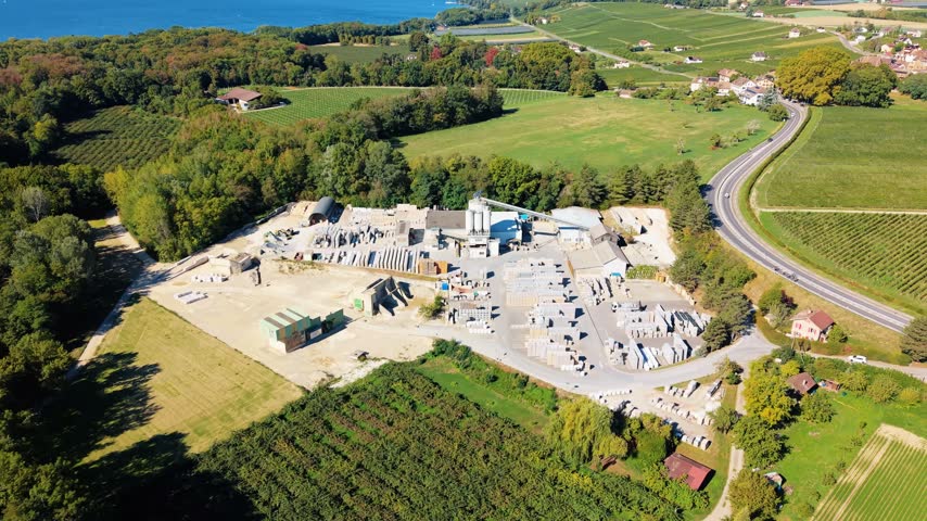 Aerial view of the Cornaz SA - Usine de Chaney industrial facility surrounded by lush green fields, vineyards, and a winding road in Allaman, Vaud, Switzerland.