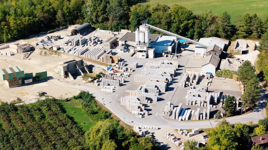 Aerial view of Cornaz SA Usine de Chaney industrial facility with concrete silos and stacks of stone blocks surrounded by trees in Allaman, Vaud, Switzerland.